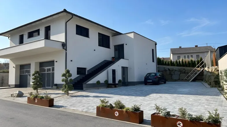Modernes Einfamilienhaus mit weißer Fassade, Doppelgarage und gepflasterter Einfahrt.