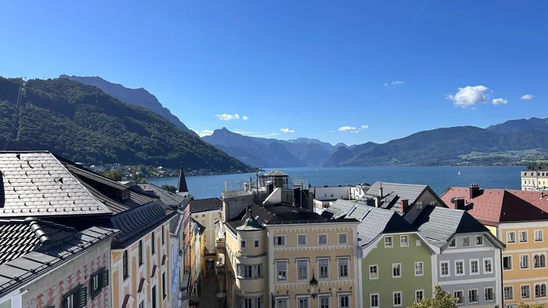 Panoramablick auf die historische Stadt, den See und die Berge unter blauem Himmel.