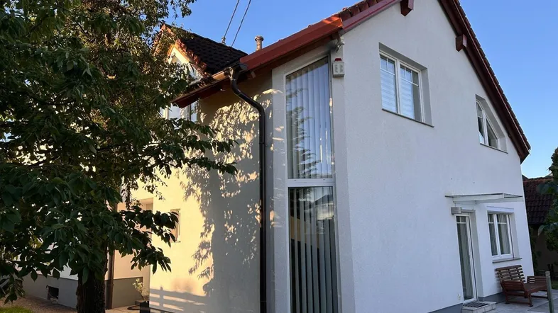Modernes Einfamilienhaus mit weißer Fassade, roten Dachziegeln und großen Fenstern im Sonnenlicht.