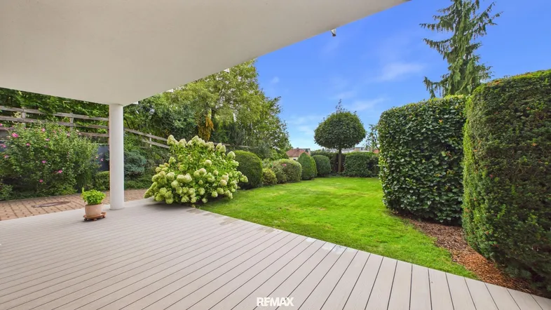 Geräumige überdachte Terrasse mit Holzdeck und Blick auf den gepflegten Garten.