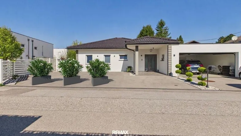 Modernes Einfamilienhaus mit weißer Fassade, dunklem Dach und integrierter Garage.