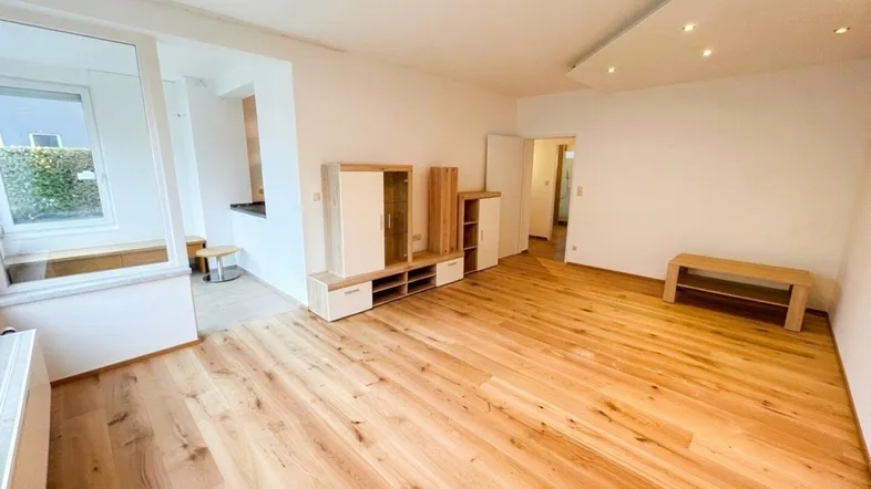 Helles Wohnzimmer mit modernem Parkettboden und integrierten Deckenleuchten, offen zu einem Essbereich.