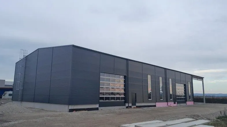 Neues Industriegebäude mit moderner dunkelgrauer Fassade und großen Glasrolltoren unter bewölktem Himmel.