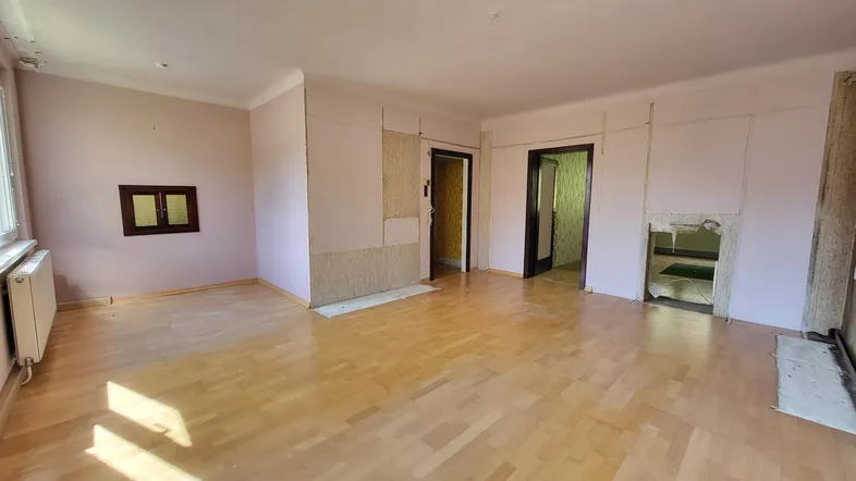 Geräumiges Wohnzimmer in Renovierung mit Parkettboden und Heizkörpern, bereit für die Neugestaltung.