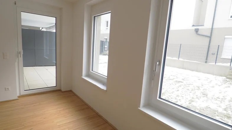 Helles Zimmer mit Parkettboden und Zugang zu einer Terrasse oder Loggia, ideal für Neubau.