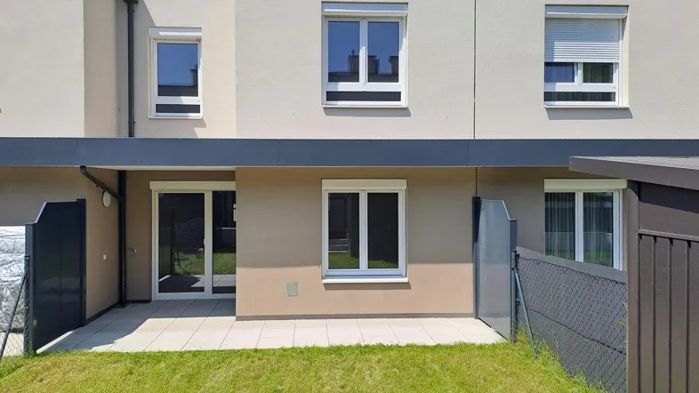 Moderne Reihenhausfassade mit kleiner Terrasse und Rasenfläche im Gartenbereich.