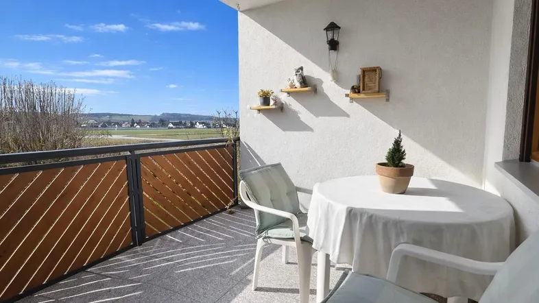 Heller Balkon mit Sitzgelegenheiten und weitem Blick ins Grüne.
