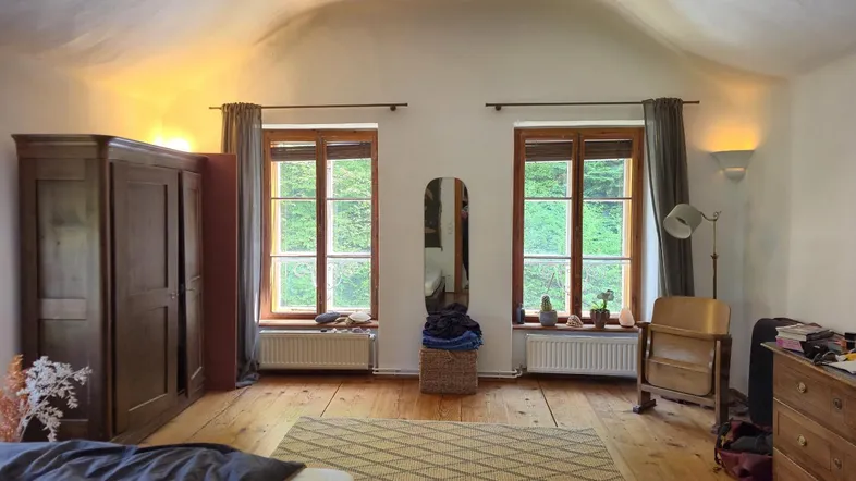Geräumiges Schlafzimmer mit Holzdielenboden, gewölbter Decke und Blick ins Grüne.