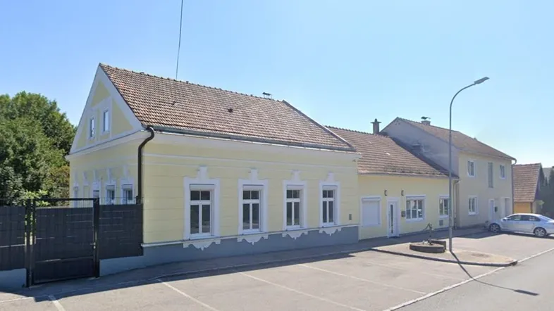 Gelbes Gebäude mit traditioneller Architektur, Satteldach und Parkplätzen davor.