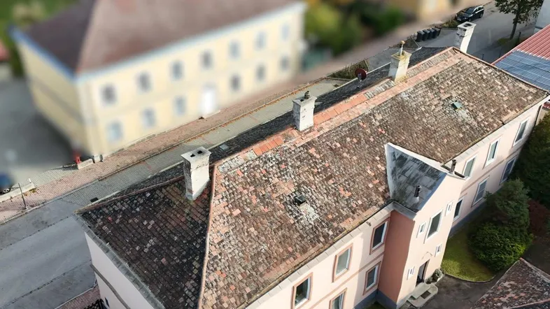 Luftaufnahme eines älteren Gebäudes mit Ziegeldach und umliegender Bebauung in ländlicher Umgebung.