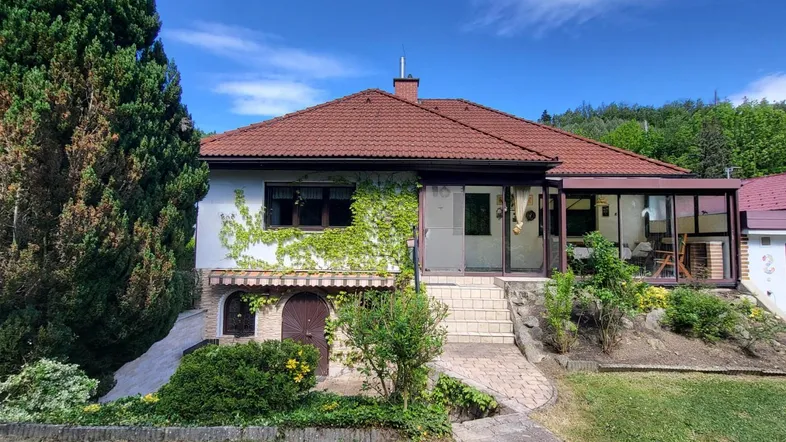 Traditionelles Haus mit rotem Ziegeldach, begrünten Fassaden und einem Wintergarten.