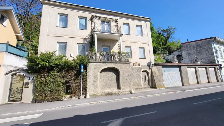 Historisches Gebäude mit mehreren Balkonen und Garagen entlang einer Straße.