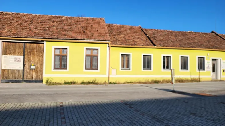 Gelbes Gebäude mit braunem Ziegeldach und Holztor unter blauem Himmel.