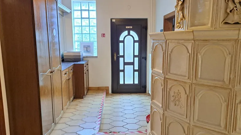 Geräumiger Flur mit traditionellem Kachelofen, Holzschränken und gefliestem Boden am Eingangsbereich.
