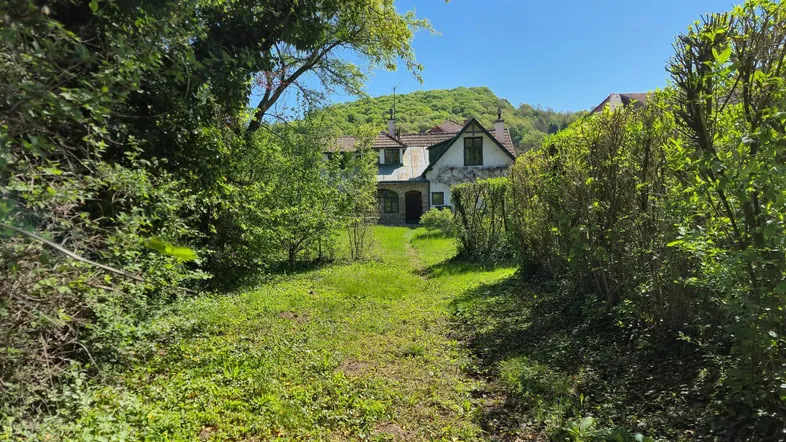 Alteres Haus umgeben von üppigem Grün und Bäumen, mit einem Pfad, der zum Eingang führt.