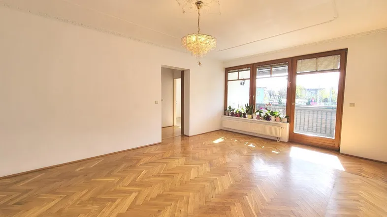 Helles Wohnzimmer mit Fischgrätparkettboden, Stuckdecke und Zugang zum Balkon.