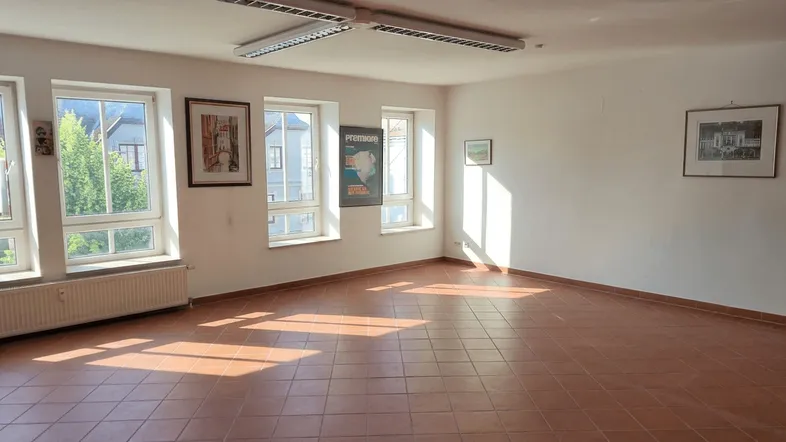Helles, leeres Zimmer mit Terrakotta-Fliesenboden und mehreren Fenstern, durch die Sonnenlicht einfällt.