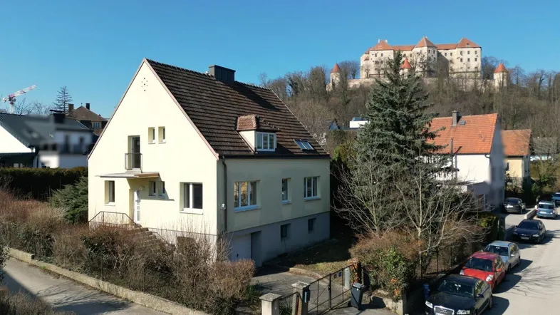 Freistehendes Haus mit Satteldach und Blick auf die historische Burg im Hintergrund.