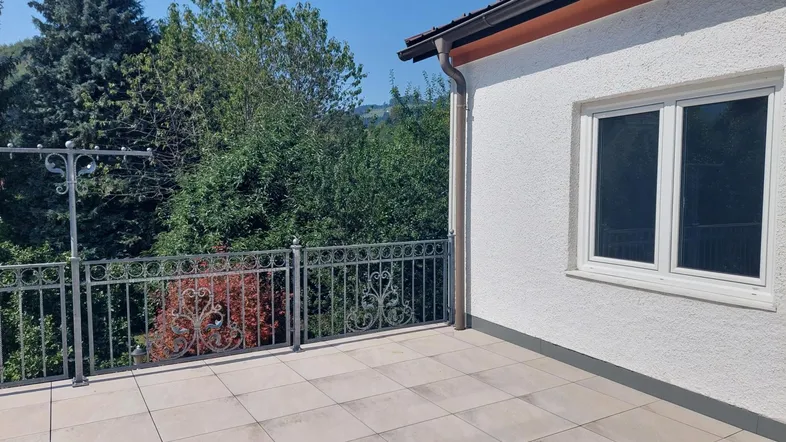 Große geflieste Terrasse mit schmiedeeisernem Geländer und weitem Blick ins Grüne.