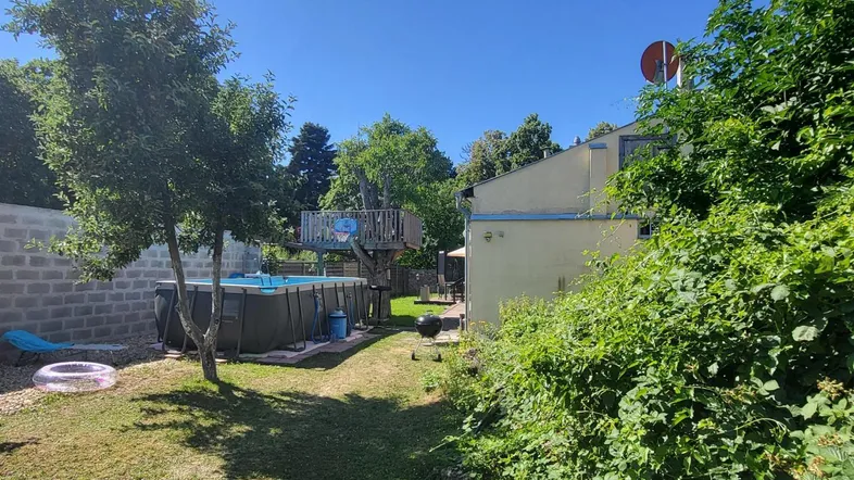 Großer Garten mit Rasenfläche, Aufstellpool und einem Baumhaus im Hintergrund unter blauem Himmel.