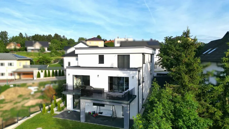 Modernes Einfamilienhaus mit weißer Fassade, Flachdach und gepflegtem Garten in grüner Umgebung.