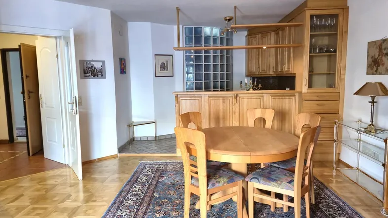 Geräumiger Wohn- und Essbereich mit Holzboden, Esstisch und integrierter Bar mit Glasbausteinen.