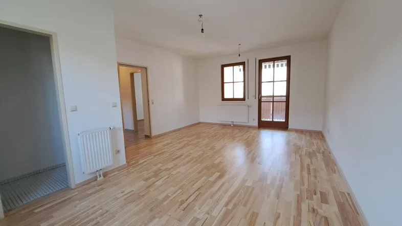 Heller, leerer Raum mit Holzboden und Zugang zu einem Balkon oder einer Terrasse.