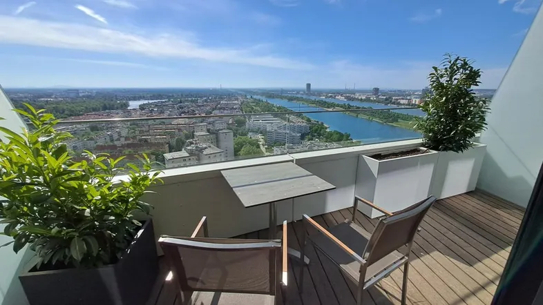 Großer Balkon mit Holzboden, Sitzgelegenheiten und weitem Blick über die Stadt und den Fluss.