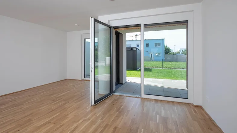 Helles Wohnzimmer mit Holzboden und Zugang zur Terrasse mit Blick ins Grüne.