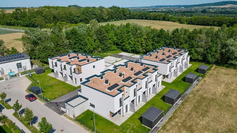 Moderne Reihenhäuser mit Flachdächern und Photovoltaikanlagen in ländlicher Umgebung mit viel Grün.