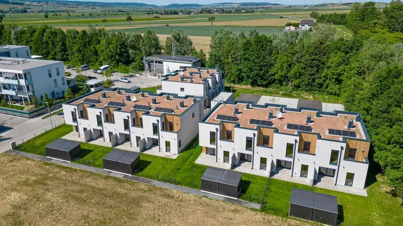 Moderne Reihenhäuser mit Flachdächern und Photovoltaikanlagen in ländlicher Umgebung mit viel Grün.