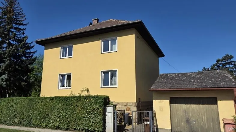 Gelbes Einfamilienhaus mit grüner Hecke, Garage und klarem blauen Himmel.