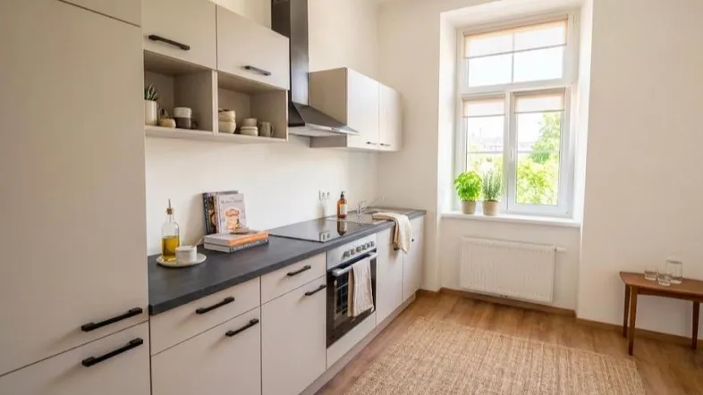 Moderne Einbauküche mit hellen Schränken, dunkler Arbeitsplatte und Fenster mit Blick ins Grüne.