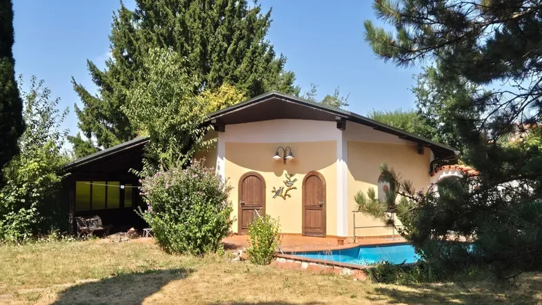 Gelbes Haus mit kleinem Poolbereich und üppiger Vegetation im Garten.