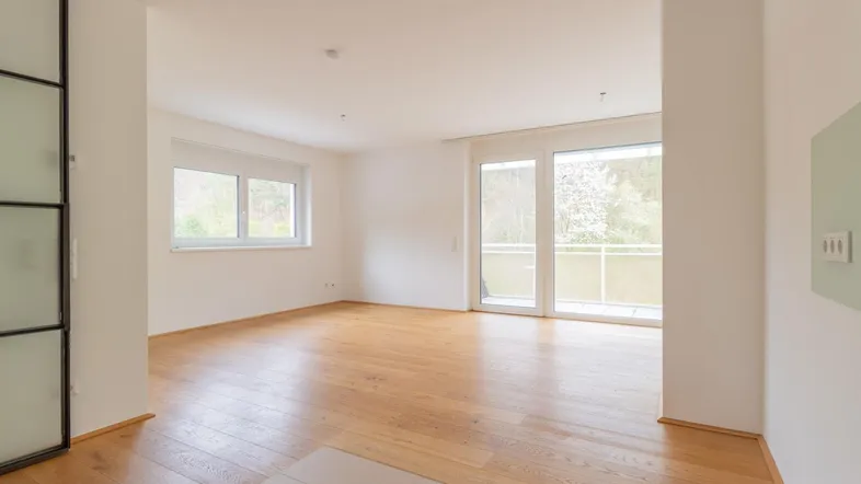 Helles, unmöbliertes Wohnzimmer mit Holzboden und Zugang zu einem kleinen Balkon.