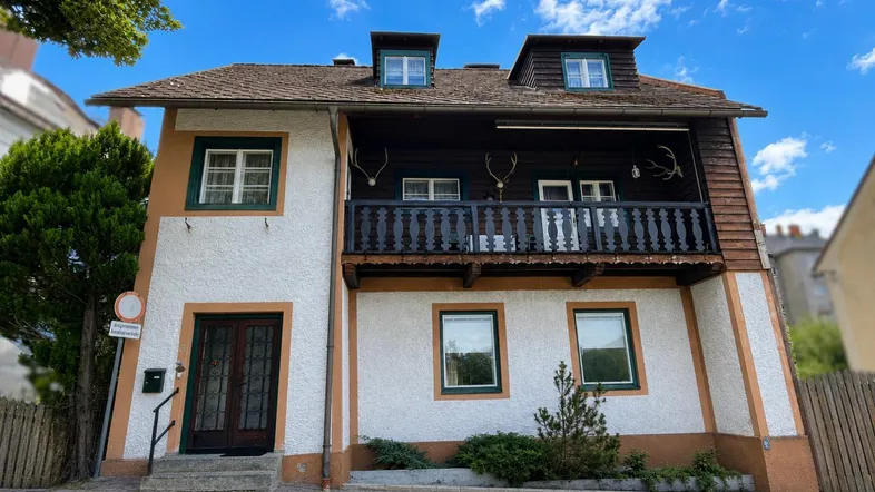 Traditionelles Haus mit weißer Fassade, Holzbalkon und dekorativen Hirschgeweihen.