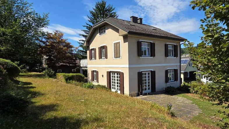 Freistehendes Haus mit heller Fassade, braunen Fensterläden und großem Gartenbereich.