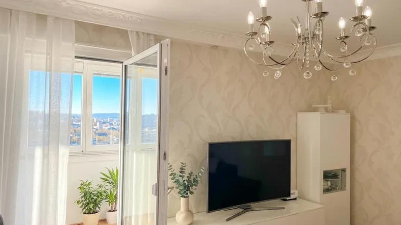 Helles Wohnzimmer mit Parkettboden, Stuckdecke und Zugang zum Balkon mit Stadtblick.
