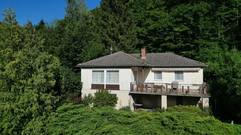 Freistehendes Haus mit Balkon und Blick ins Grüne, umgeben von üppiger Vegetation.