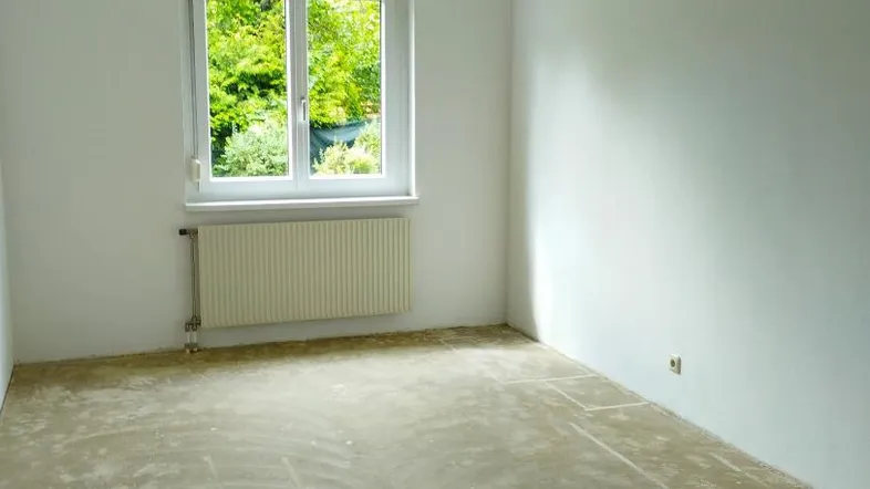Leerer Raum mit weißen Wänden, Fenster und unfertigem Bodenbelag, bereit für die Gestaltung.