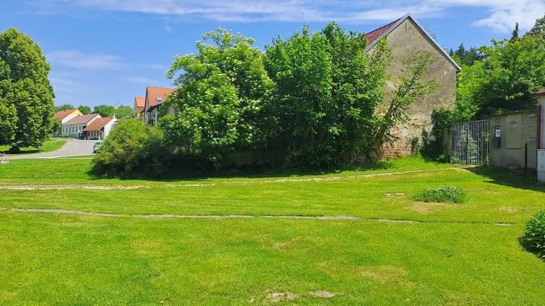 Weitläufige Grünfläche mit altem Gebäude im Hintergrund und Bäumen unter blauem Himmel.