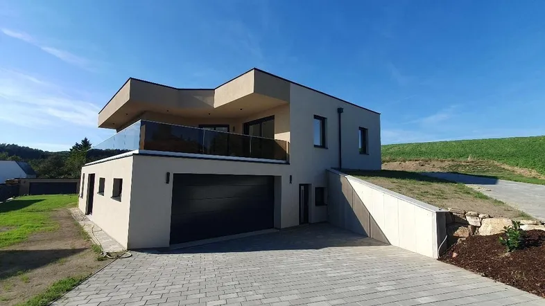Moderne Architektur eines Neubaus mit Doppelgarage, Glasbalkon und gepflasterter Auffahrt.