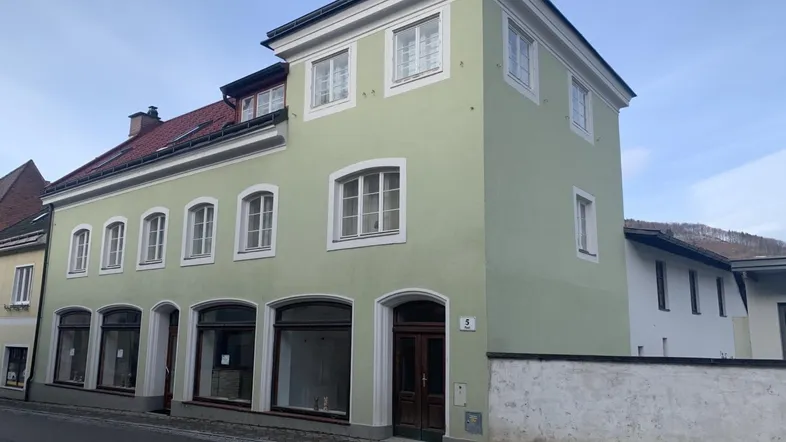 Traditionelles Gebäude mit hellgrüner Fassade, mehreren Fenstern und einem Eingangsbereich zur Straße.