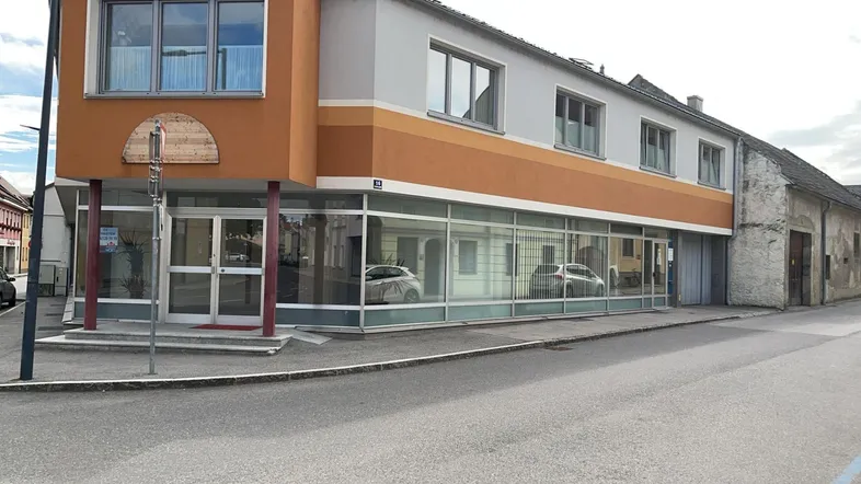 Gebäude mit großen Schaufenstern im Erdgeschoss und Wohnungen darüber an einer belebten Straße.