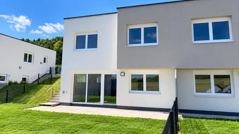 Moderne Reihenhäuser mit privatem Gartenbereich und Terrasse unter blauem Himmel.