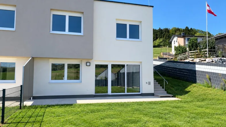 Modernes Reihenhaus mit Garten, Terrasse und Blick auf die umliegende Landschaft.