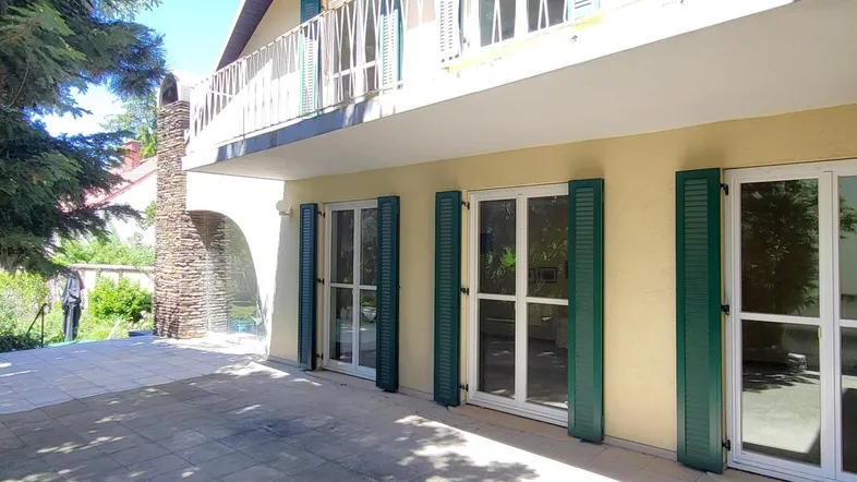 Große gepflasterte Terrasse vor dem Haus mit Zugang zu den Innenräumen und einem Balkon darüber.