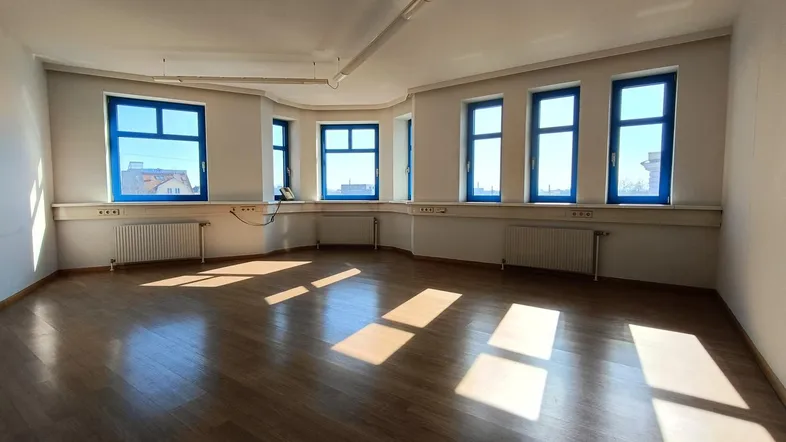 Geräumiges Büro mit vielen Fenstern, Holzboden und viel natürlichem Licht, ideal für Arbeitsbereiche.