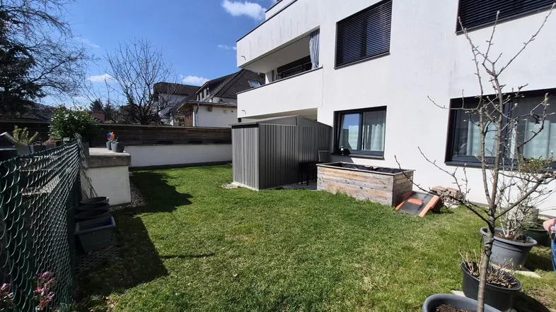 Gepflegter Gartenbereich mit Rasenfläche und kleinem Geräteschuppen neben dem Gebäude.