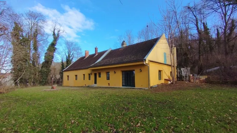 Gelbes Haus mit Satteldach und großem Gartenbereich unter blauem Himmel.